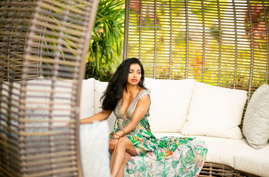 A woman in a floral dress sitting on a white, wicker outdoor couch